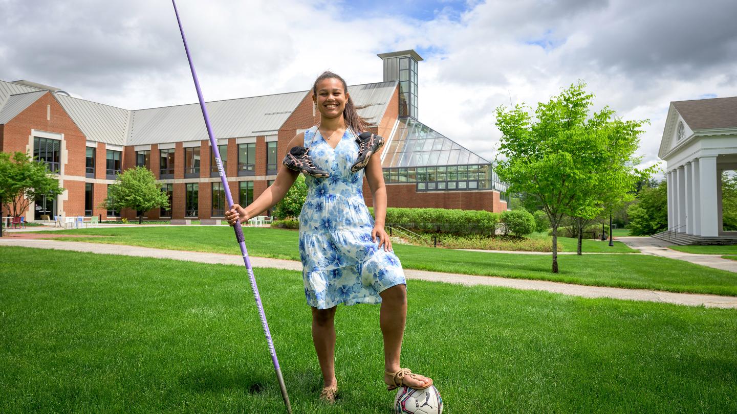 Cami Capdevila posing with javelin, soccer ball and cleats in front of Lindsay Center